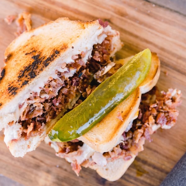 Grilled sandwich with meat, cheese, and a pickle spear on a wooden board.