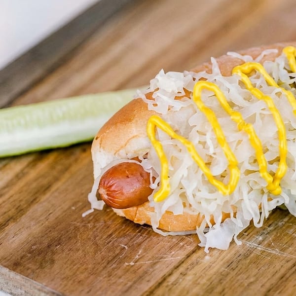 Hot dog with sauerkraut and mustard on a wooden board with a pickle spear.